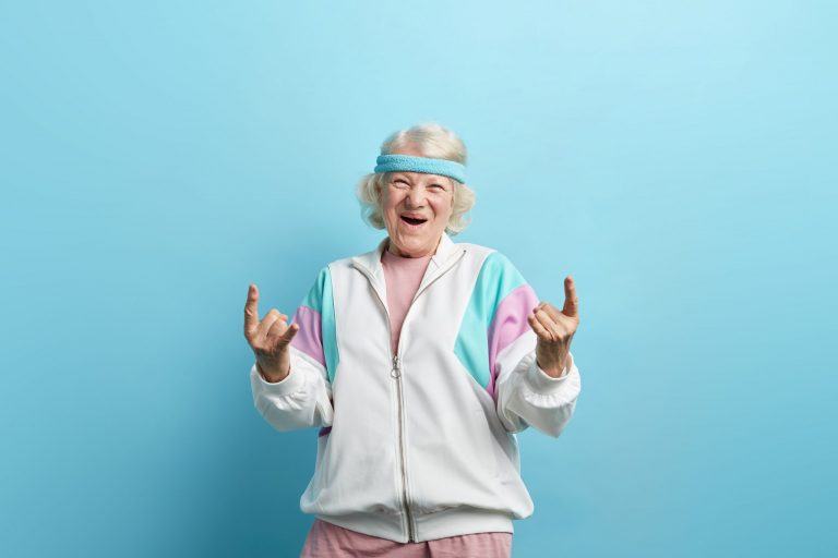 Cute hipster grandmother smiling and making rock sign against blue background