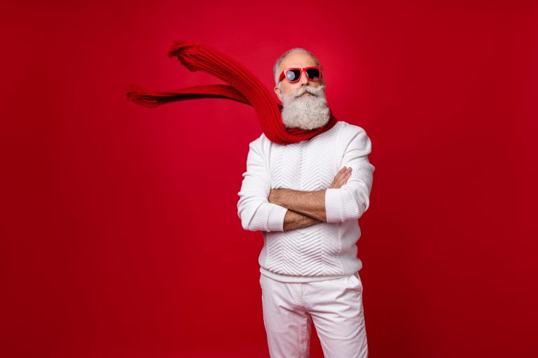 Trendy grey-haired superhero santa wear sun specs knitted clothes isolated red background