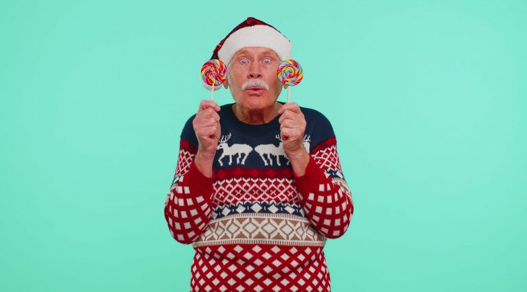 Grandfather in Christmas sweater holding candy striped lollipops hiding behind them, fooling around