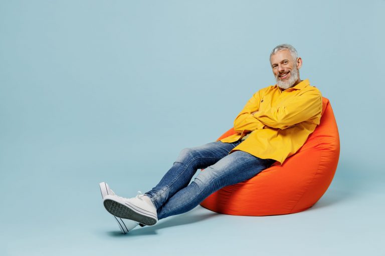 Full body smiling elderly gray-haired mustache bearded man 50s wear yellow shirt sit in bag chair look camera isolated on plain pastel light blue background studio portrait. People lifestyle concept