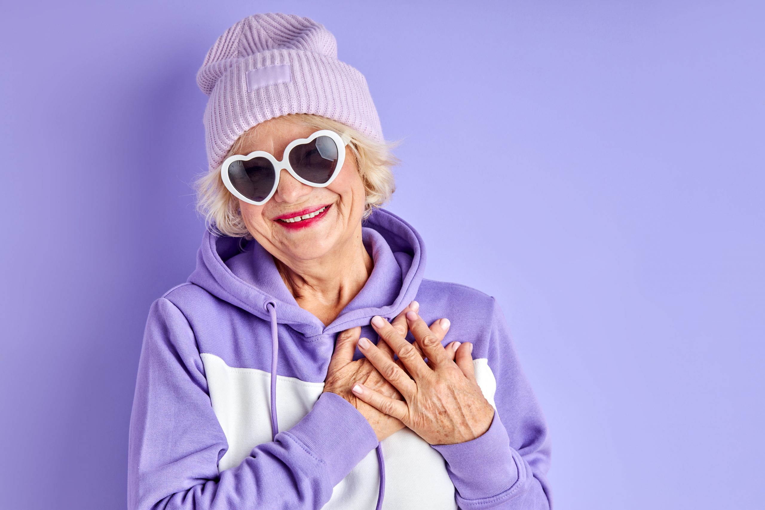 happy positive elderly woman holding hands on chest smiles