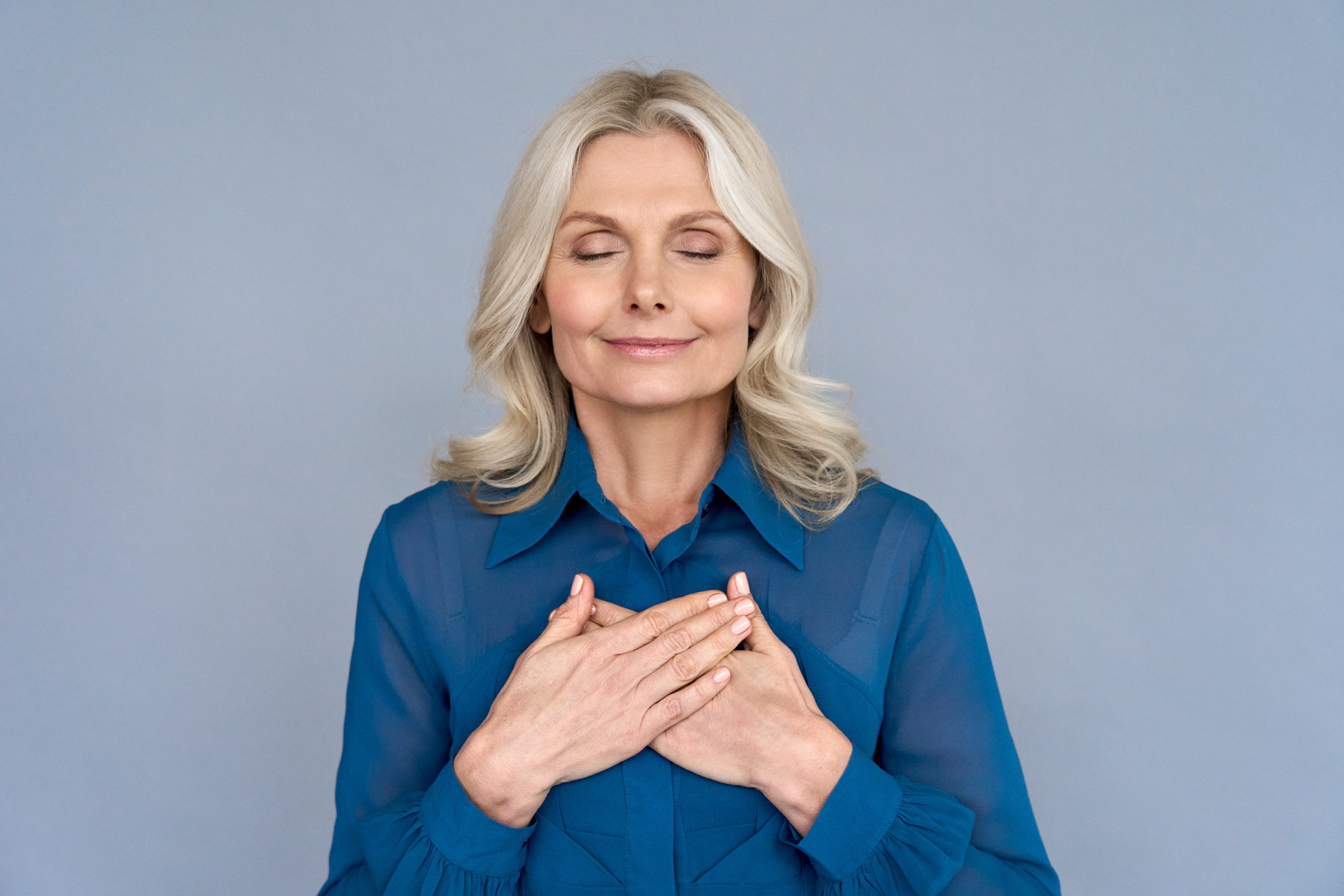 Happy mindful thankful middle aged old woman holding hands on chest