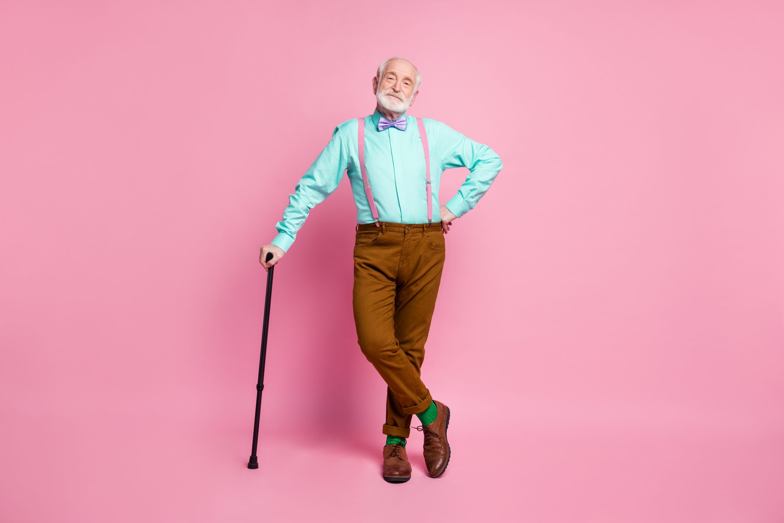 Full length photo of attractive grandpa good mood stand confident lean walking stick wear mint shirt suspenders bow tie brown pants boots green socks isolated pink pastel background