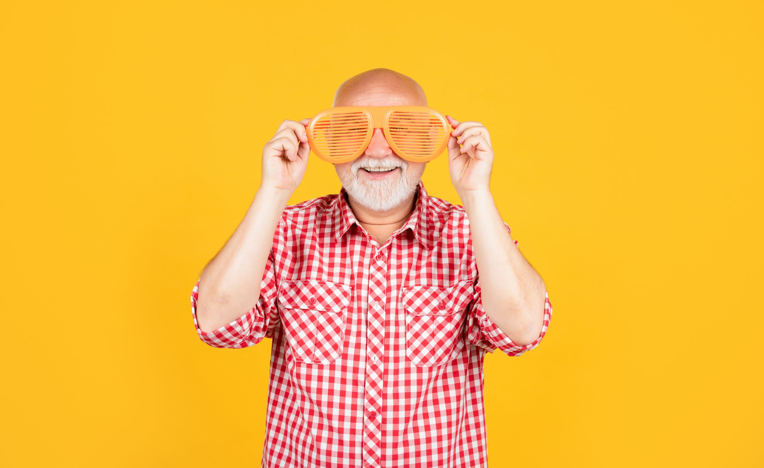 smiling old man in checkered shirt with party glasses on yellow background